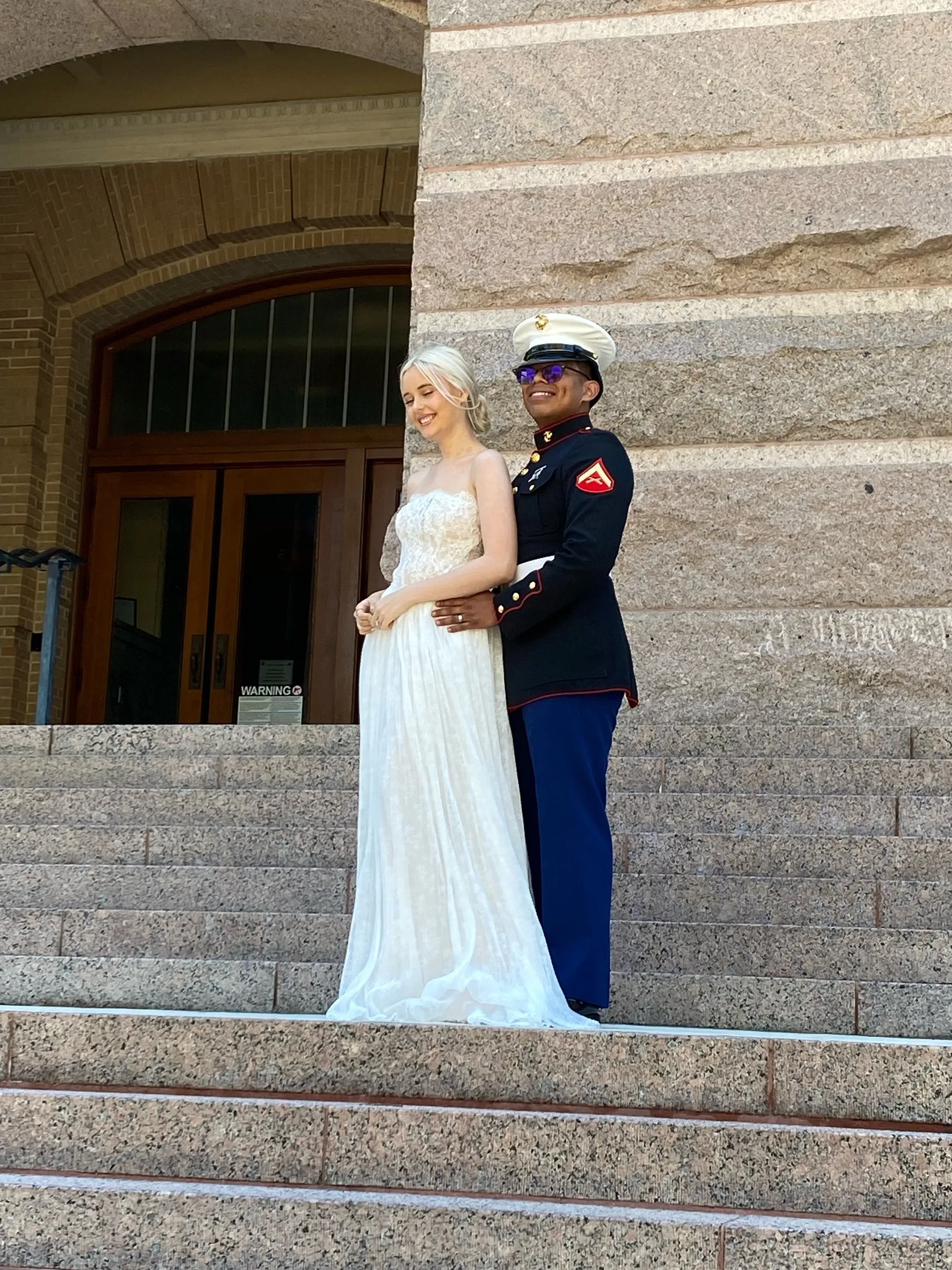 Newlyweds, one wearing a wedding dress and one a military uniform, on the steps of the 1910 Harris County Courthouse