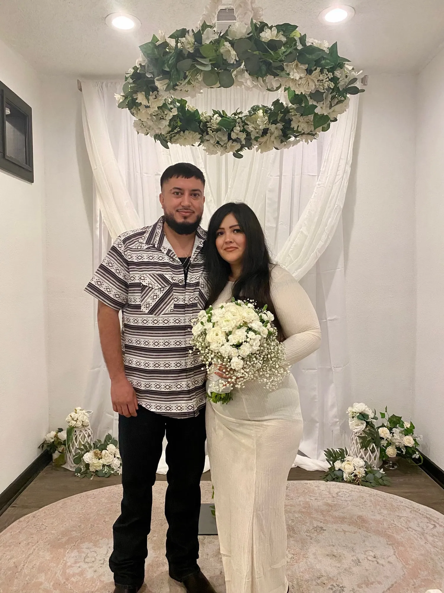 Newlywed couple with a bouquet standing beneath a floral ring at the new Twin Flames Heights office